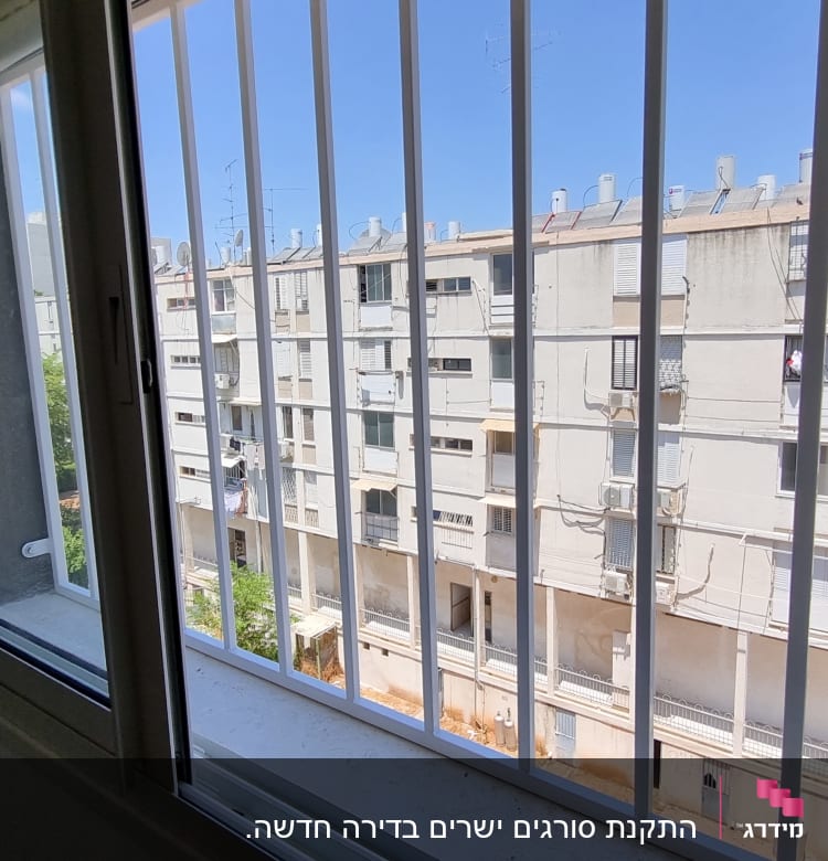 חלון פתוח עם סורגים לבנים מול בניין מגורים
